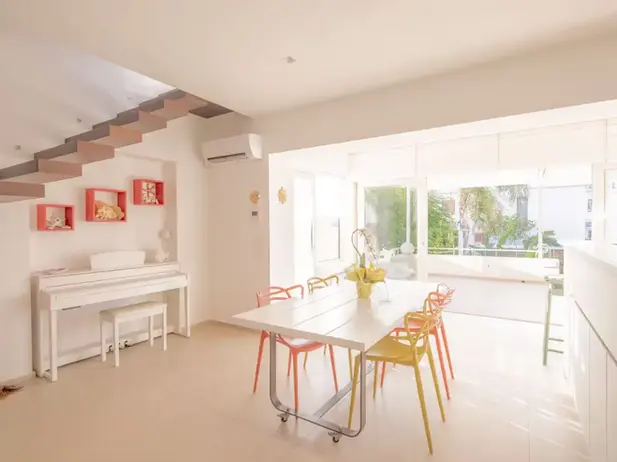 Luminosa sala da pranzo moderna, sedie colorate, pianoforte bianco, ampie finestre.