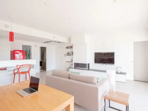 Soggiorno moderno luminoso con divano, laptop su tavolo, caminetto e TV.