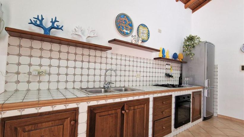 Cucina con armadi in legno e piastrelle bianche. Ville deluxe con piscina Castellammare del Golfo.