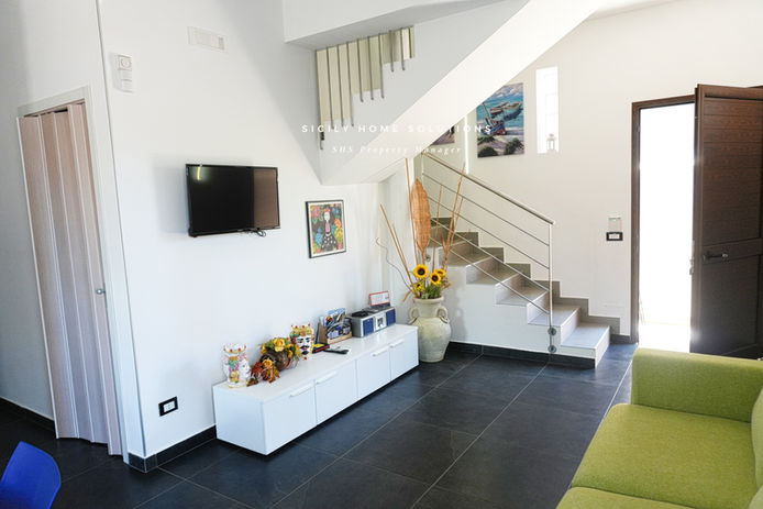 Soggiorno con TV, scala, fiori e mobili bianchi; ville deluxe con piscina castellammare del golfo.