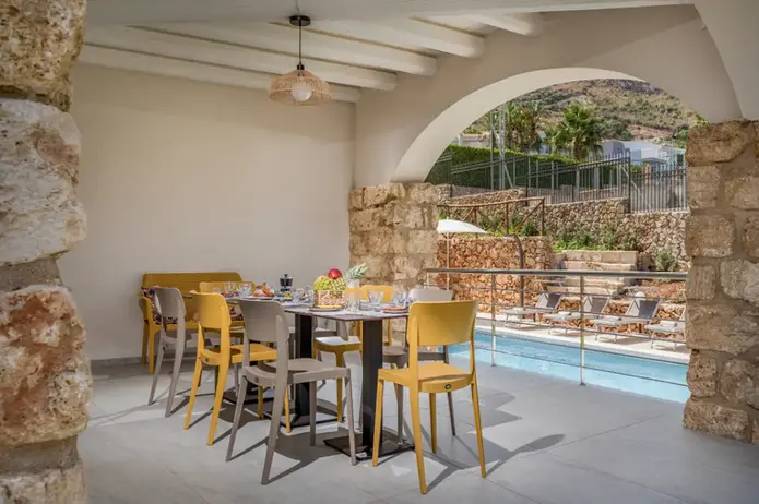 Tavolo da pranzo all'aperto sotto un portico, vista piscina e colline.