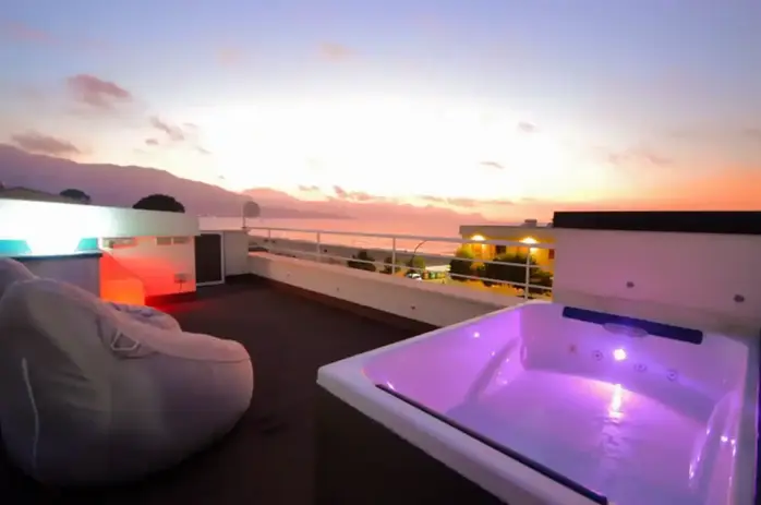 Terrazza panoramica con jacuzzi illuminata, vista mare al tramonto.