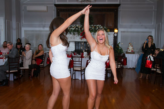 Two girls in white dresses dance joyfully at a Sweet 16 party.