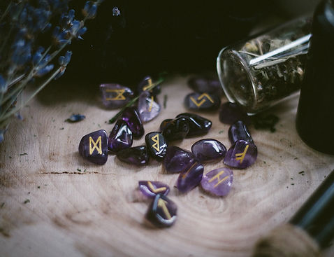 Amethyst gemstones with gold runes on them spilled from a glass container onto a wooden table
