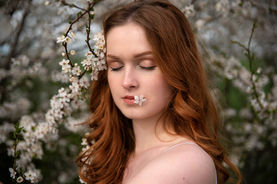 rusovlasá dívka se zavřenýma očima drží mezi rty bílý květ, portrét v jarní přírodě