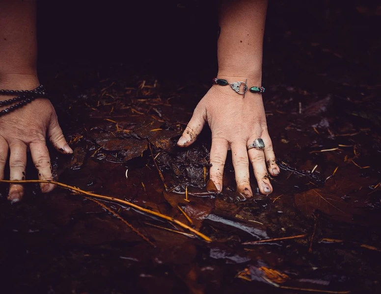 Spirit Portals program cover image hands touching the earth with brown autumn dead leaves near water