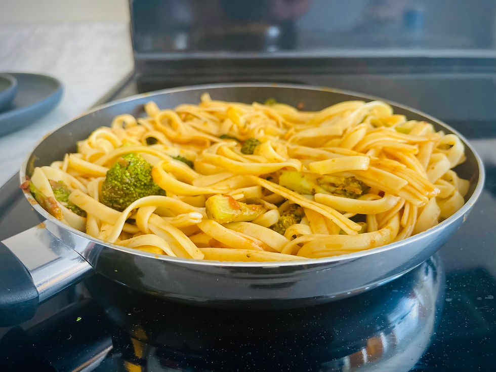 Fettuccine with broccoli in a skillet on a stove. The pasta is lightly sauced, creating a warm and inviting culinary scene.