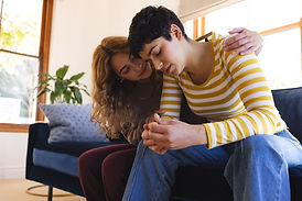 Sad biracial lesbian couple embracing and comforting, sitting on couch in sunny living roo