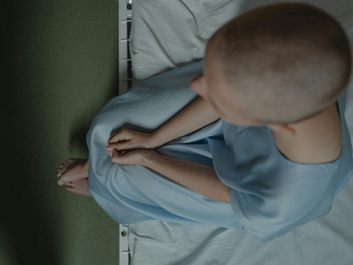 A lady with a disease sitting anxiously on a hospital bed wearing a blue hospital gown.