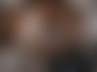 A woman sitting on a rug in a dimly lit, cozy bedroom, looking down with a focused expression while gripping and wringing a white towel with both hands to physically release nervous system tension.