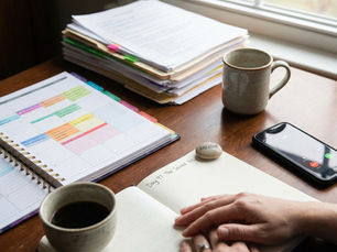 A person's hands resting gently on an open journal that reads "Day 97: The Sacred Yes" with a small stone saying "Breathe." A ringing smartphone, a color-coded planner, and a stack of papers sit on the wooden desk, representing the pause and grounding needed to overcome a nervous system freeze before taking a difficult phone call.