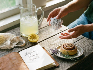 Person tearing up a “career path” note beside lemonade, journal reading “Life’s Scenic Route,” and pastry, symbolizing dealing with disappointment and embracing life’s unexpected redirection