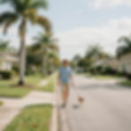 Man walks dog on residential street with palm trees