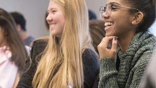 A photo of students laughing in a classroom and taking notes
