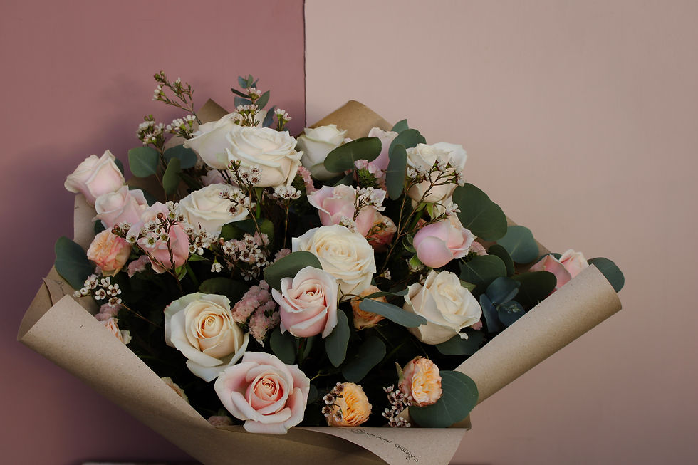 Elegant bouquet of blush and delicate pink roses and greenery, wrapped in craft paper, against a soft pink wall