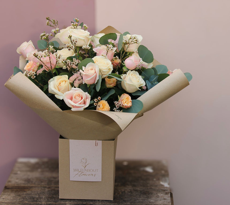 Rose bouquet with blush tones, eucalyptus, in craft box, branded 'Wild About Flowers', on wood surface, pink wall background