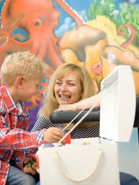 Junge wählt Spielzeug aus Belohnungsbox, lächelnde Frau vor Unterwasser-Wandbild.