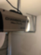 Chamberlain Whisper Drive Plus garage door opener with "3/4 HPS" text in a garage. Metal railings visible in the background.