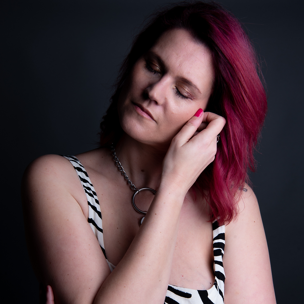 Une femme aux cheveux roses, dans une pose pensive, vêtue d'une robe à motif zèbre et portant un collier en chaîne argentée, dégageant une atmosphère de calme et de réflexion.