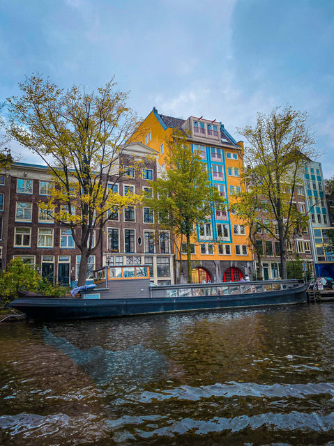 Historic buildings and trees lining a canal with a boat in Amsterdam. Boat is AMA Waterways River Cruise.
