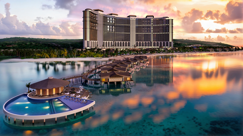 Luxury beachfront view of Moon Palace Grand featuring overwater bungalows, a large resort building, and calm ocean waters at sunset.