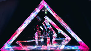 Visitors walking through a triangular, walk-in installation with projections on walls and floor at AYA Universe Dubai.