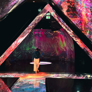 A person standing inside a dark room surrounded by abstract projections covering walls and floor at AYA Universe Dubai.