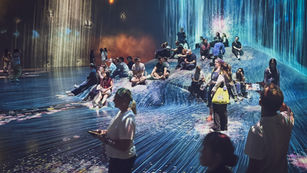 People sitting and walking through immersive digital waterfall projections at teamLab Borderless Tokyo