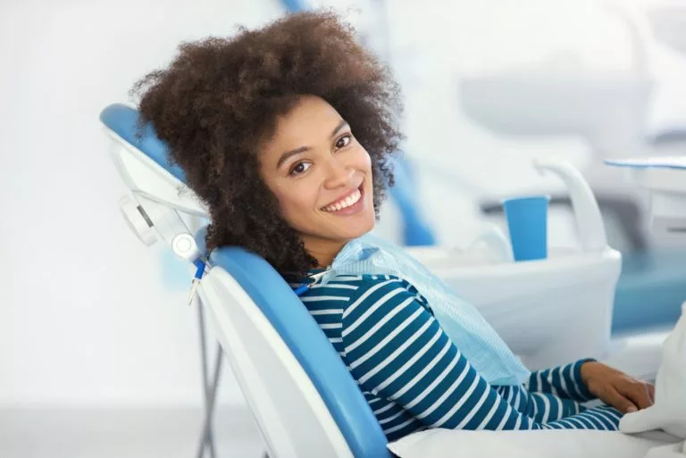woman_with_black_hair_sitting_in_dental_chair_looking_at_camera_and_smiling-768x513.webp