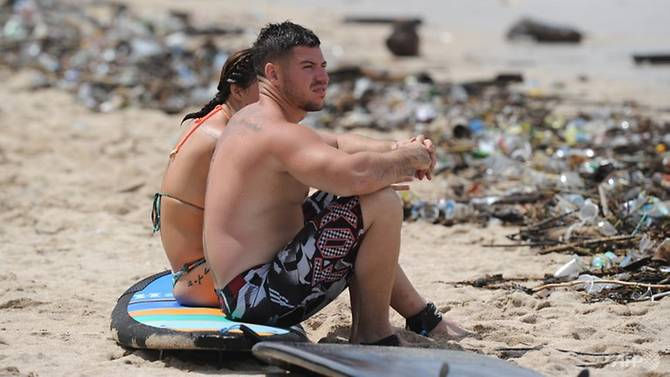 Tourists sit on a surfboard along Kuta beach, surrounded by debris and rubbish washed up by the tide Read more at https://www.strawmansg.com/blog/anti-plastic-straw-wave-has-struck-bali-as-government-bans-single-use-plastics