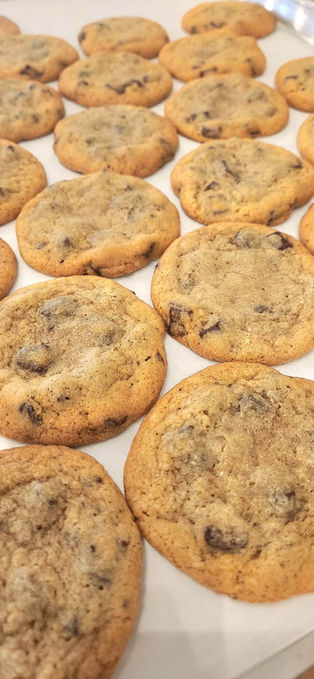Freshly baked golden brown chocolate chip cookies arranged on baking sheet.