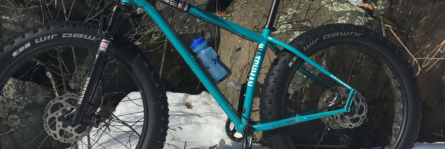 Teal bike leaning on a rock with snow all around.