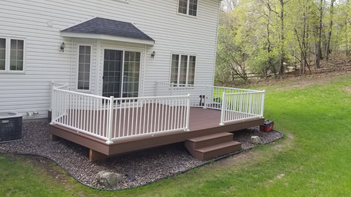 New deck with white rails on a white house with a bay window sliding door.