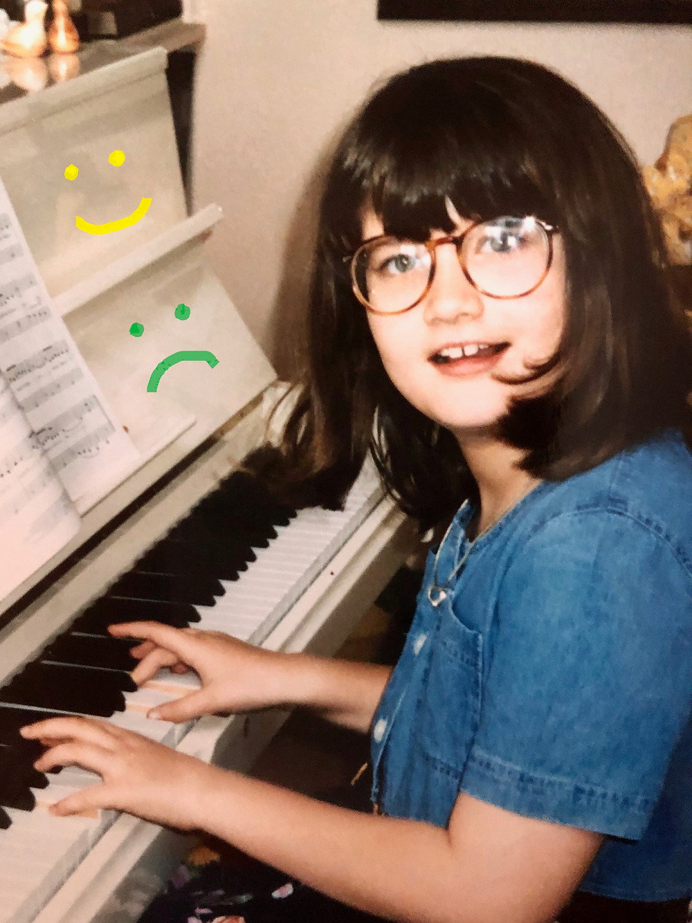 white girl with glasses and brown hair playing a white piano with handdrawn frowny faces on piano