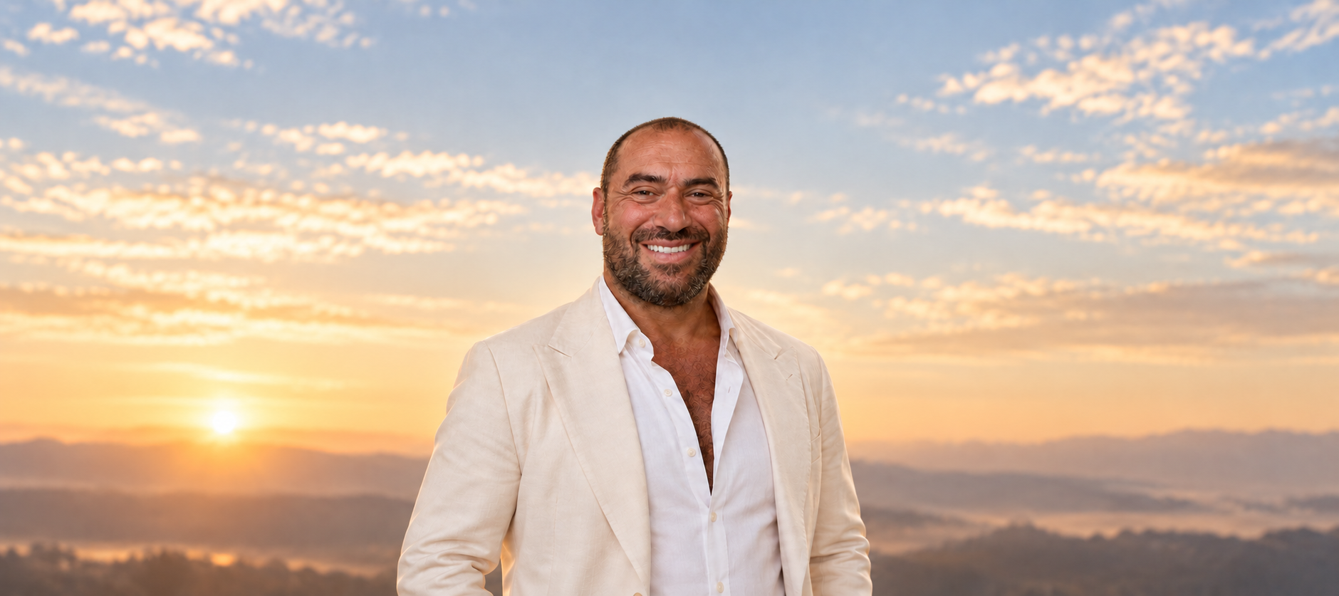 Niko-Helios in an ivory suit against a warm dawn sky, with soft natural light