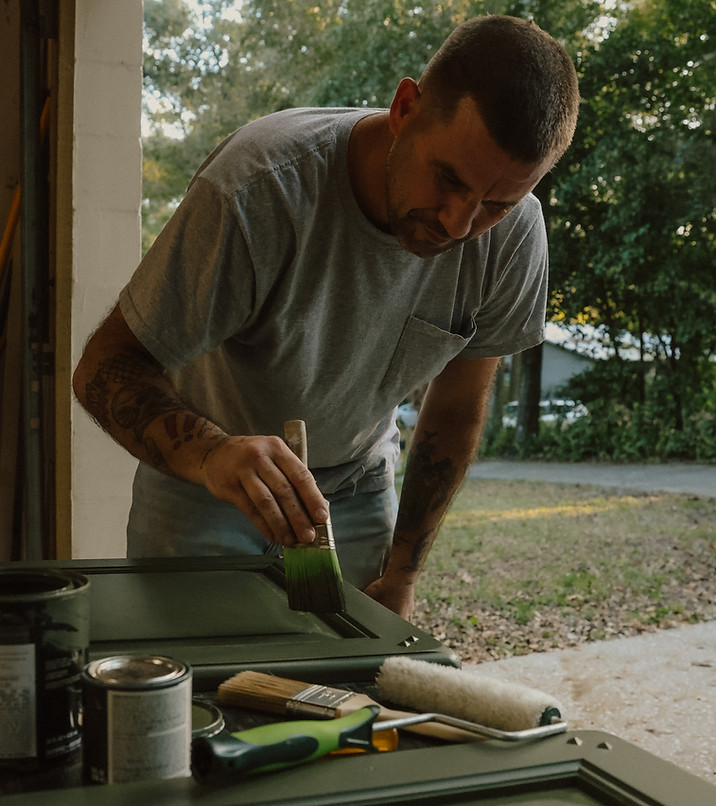 A person works in a garage, bent over and painting 