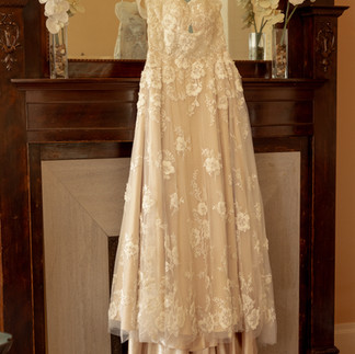 A wedding dress hangs from a hanger in front of a fire place.