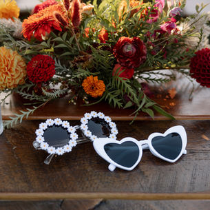 A table with the bride and grooms sunglasses and wedding florals.