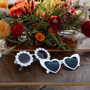 A table with the bride and grooms sunglasses and wedding florals.