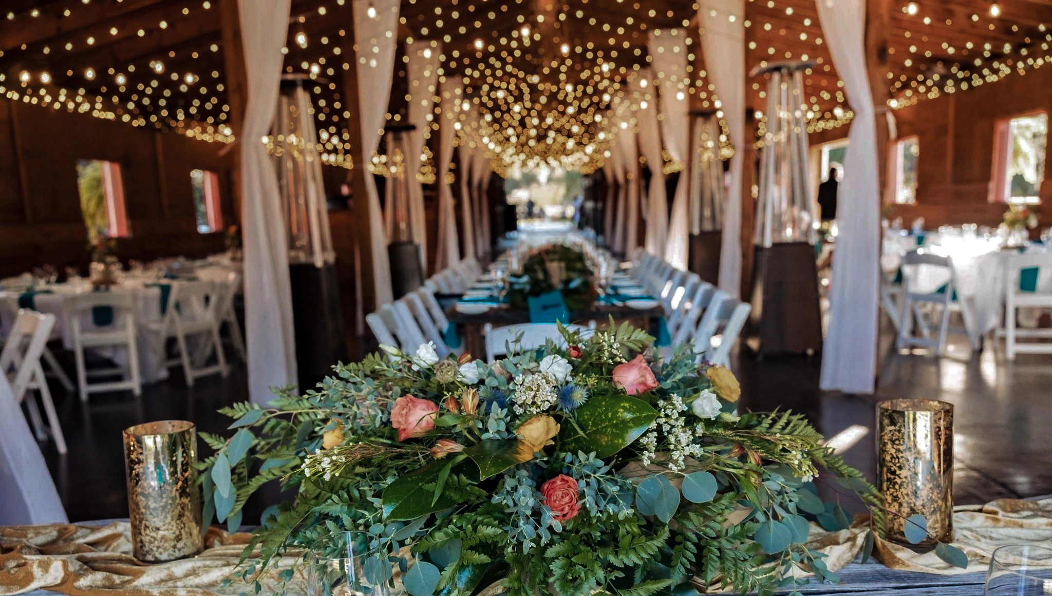 wedding decor includes floral centerpieces and twinkle lights hung from the ceiling from the traditional Barn for a wedding reception at Red Gate Farms