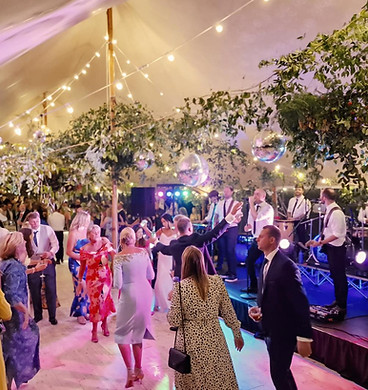 Wedding guests dancing under string lights and foliage with a live band in a marquee