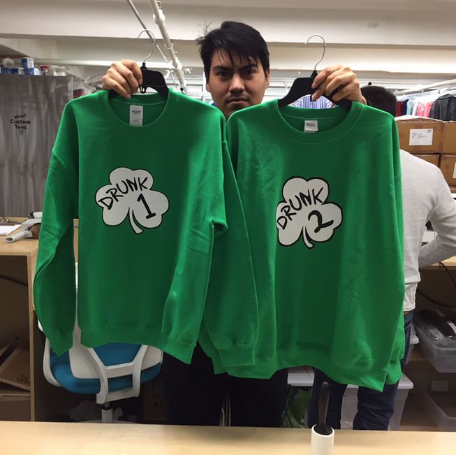 Two green shamrock 'Drunk 1' and 'Drunk 2' designs on custom screen printing sweatshirts and custom crewneck sweatshirts in a shop. At Wow! Custom Tees