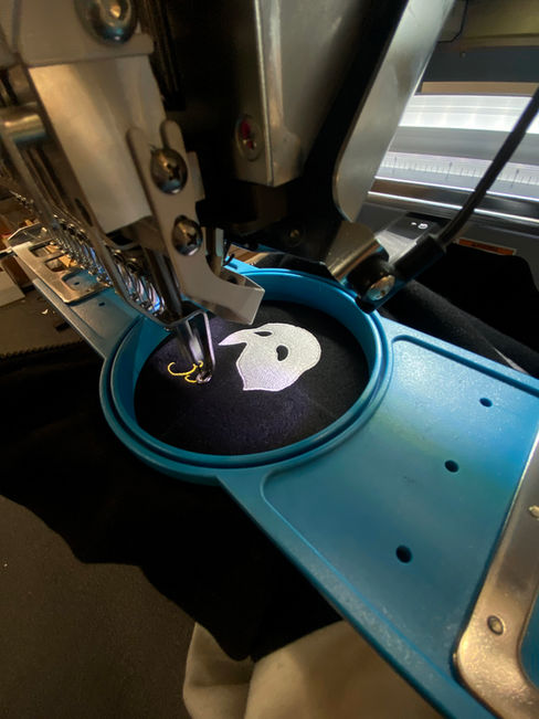 Close-up of an embroidery machine stitching a ghost logo on fabric for custom embroidered zip up hoodies and premium custom zip up hoodies. At Wow! Custom Tees