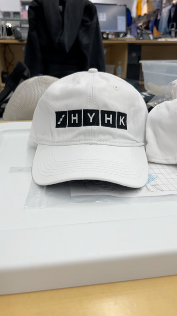 White HYHK embroidered baseball hat on a worktable; sleek custom baseball hat with black block-letter patches in a studio setting. At Wow! Custom Tees