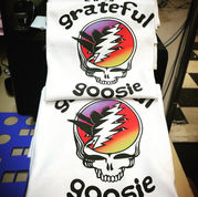 Stack of white tees with Grateful Goosie skull and rainbow lightning, made via screen printing nyc; promo for custom t shirts no minimum. At Wow! Custom Tees