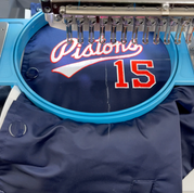 Embroidery machine stitching 'Pistons 15' on an embroidered varsity jacket, highlighting quality craftsmanship for custom varsity jackets. At Wow! Custom Tees