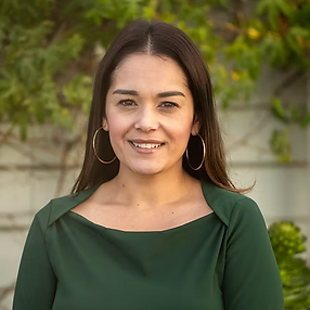 Headshot of Nohemy Chavez, Community College Counselor Training Coordinator. A woman with long dark hair and gold hoop earrings smiles, wearing a dark green top against a blurred green foliage background.