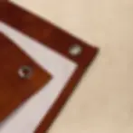 Close-up of tapestry corner showing double-fold hem and silver iron grommet on rust-brown fabric with autumn floral print.