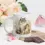 Thumbnail: White ceramic cat mug with floral illustration placed among flowers, sweets, and paper elements on a light surface