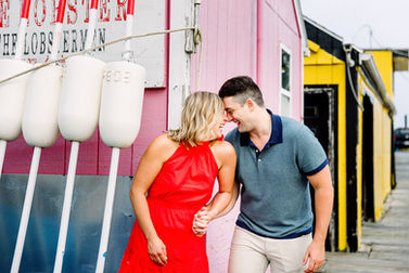 Engaged couple by a pink building with white buoys at Widgetty Wharf in Portland Maine
